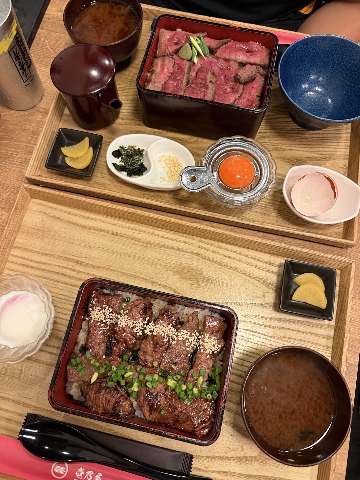 2種のステーキ重セットが木製トレーに並んだ俯瞰。レアの赤い断面と醤油タレがかかった牛肉が対比する